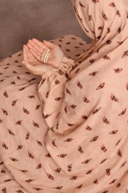 Close-up of a person wearing a light pink dress with a subtle pattern, holding a phone.