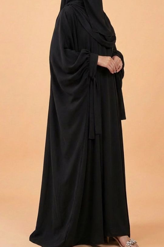 Person wearing a black abaya against a beige background