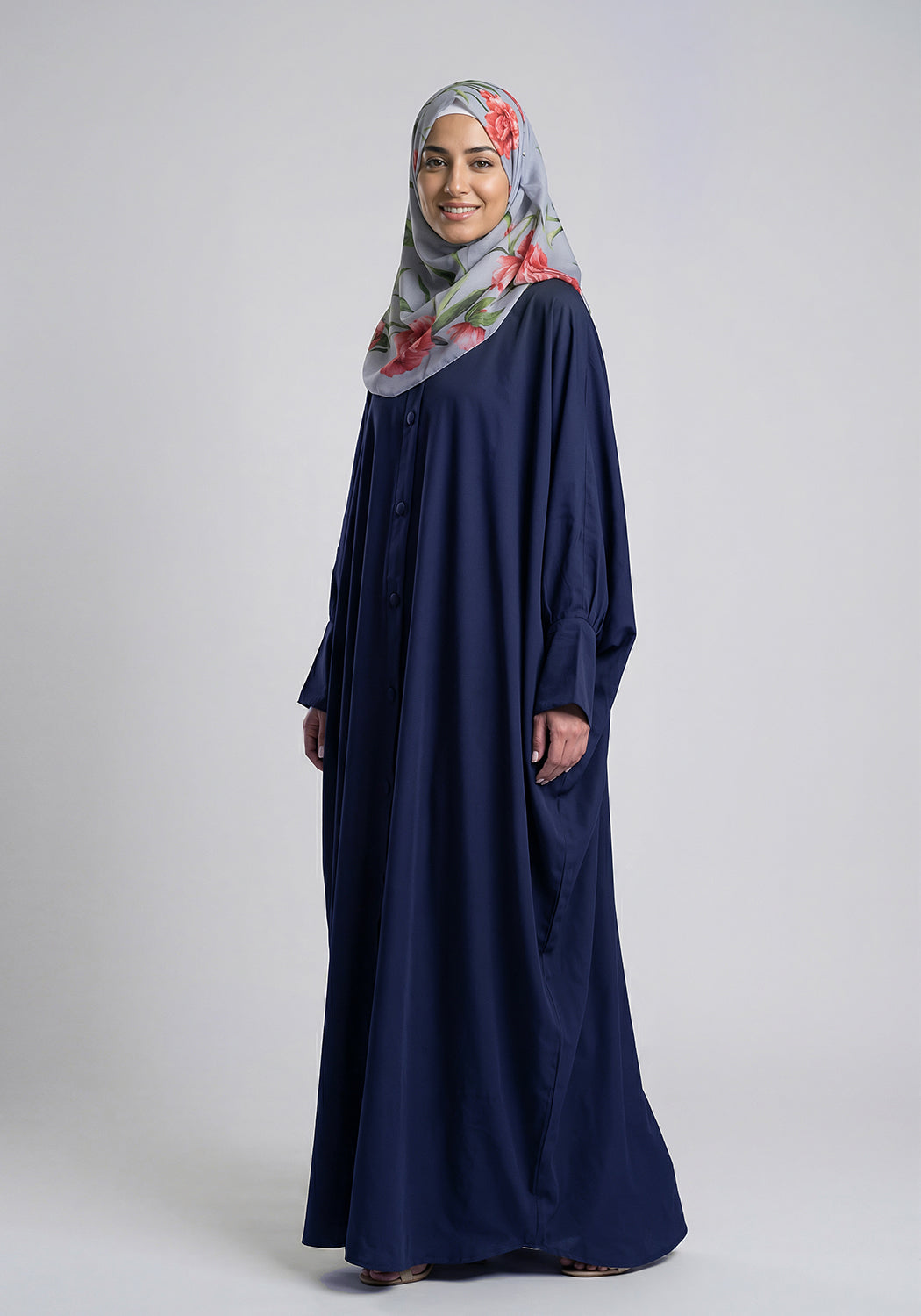 Woman wearing a navy blue abaya and a floral hijab on a white background